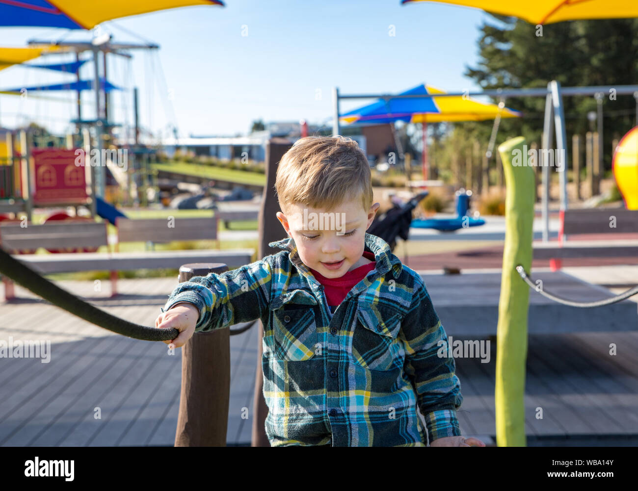 Ein kleiner Junge sorgfältig Praktiken, die über die Hängebrücke auf dem Spielplatz fort Stockfoto