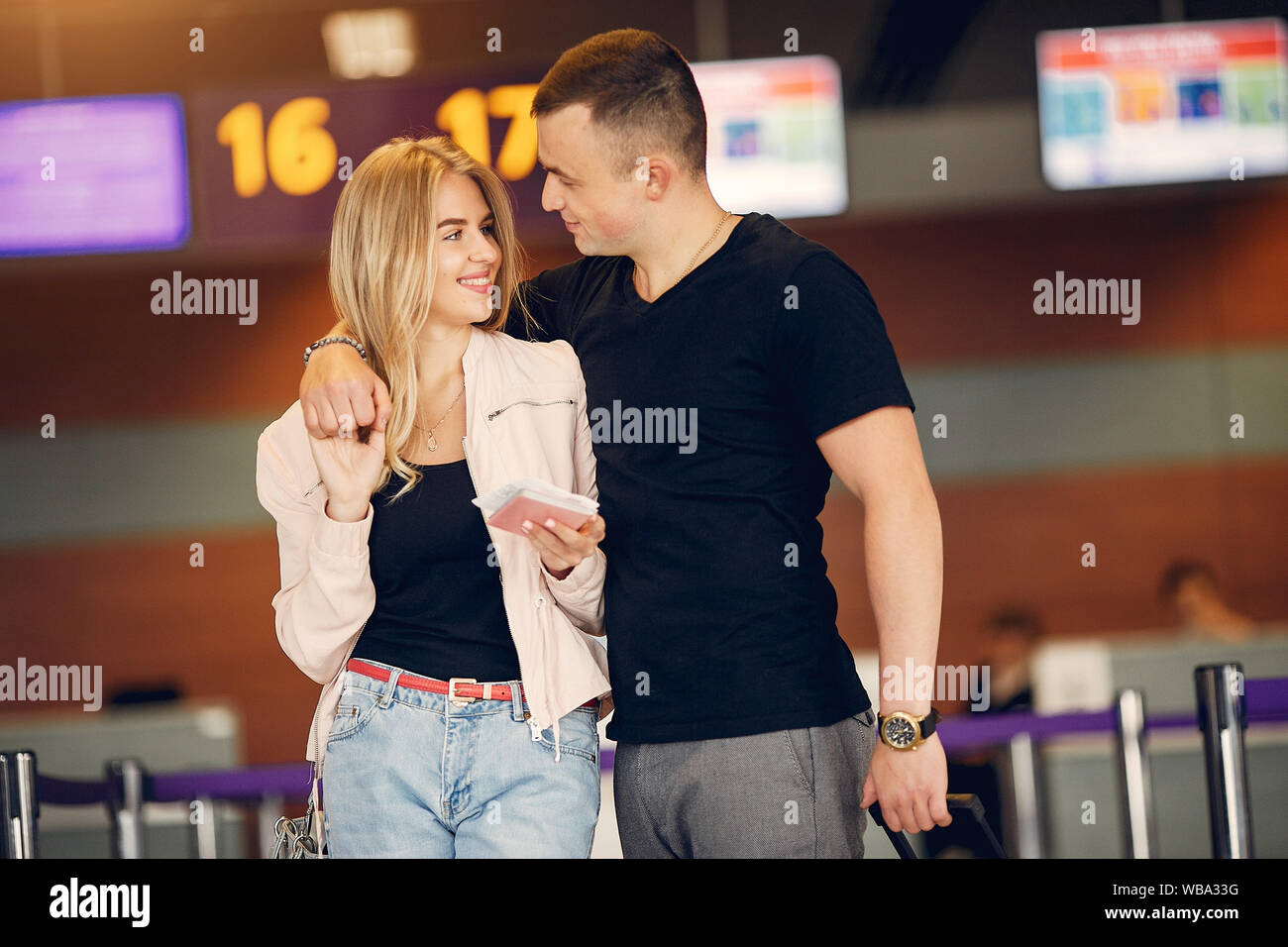 Paar in einem Flughafen. Schöne Blondine in einem weißen Mantel. Mann in einem schwarzen T-Shirt Stockfoto