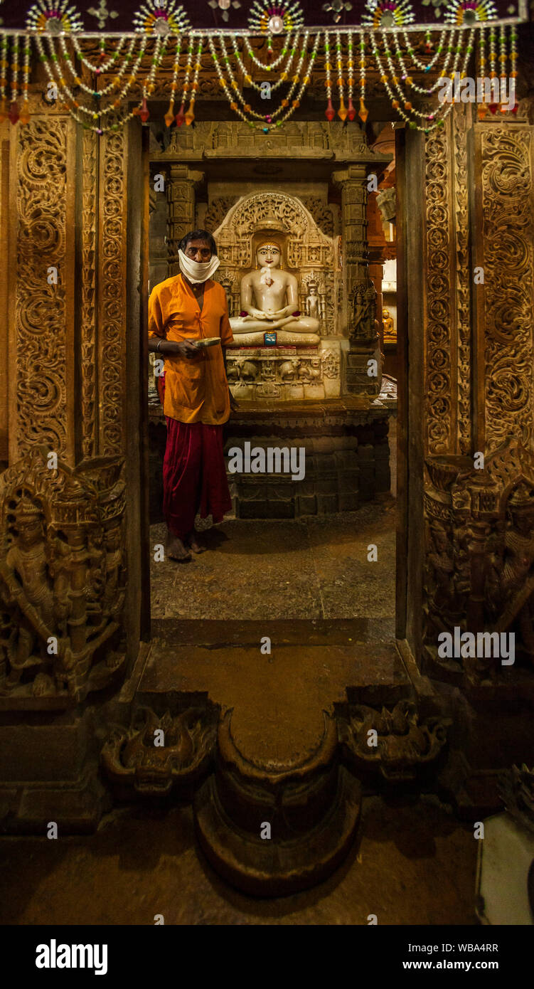 Ein Mann steht in der inneren Kammer dieses Jain Tempel unter monetären Angebote in einem Jain Tempel in Jaisalmer Fort, Indien. Stockfoto