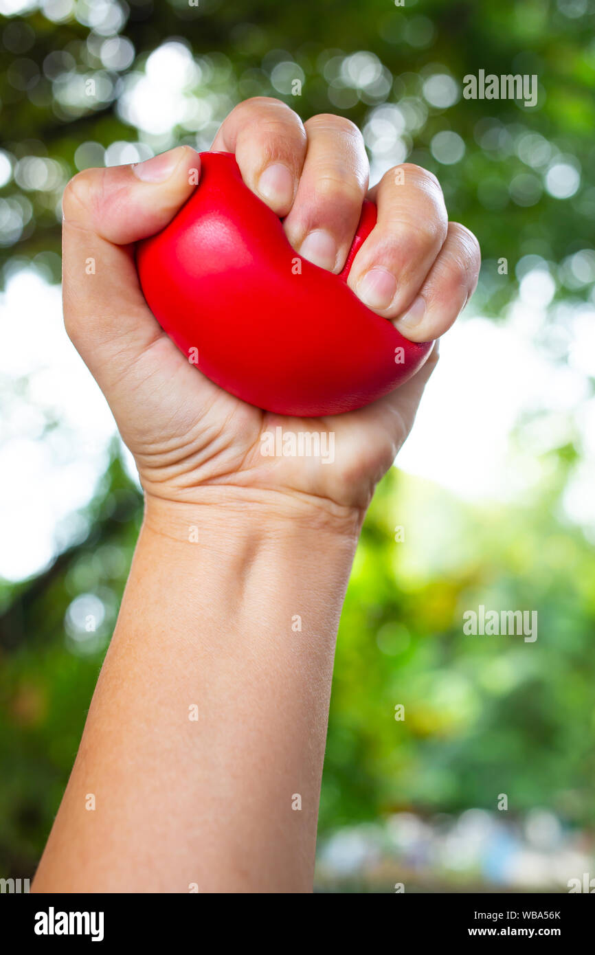 Frau linke Hand zusammendrücken rot Stress Ball auf Bokeh grünen Garten Hintergrund, Übung und Massage Konzept Stockfoto