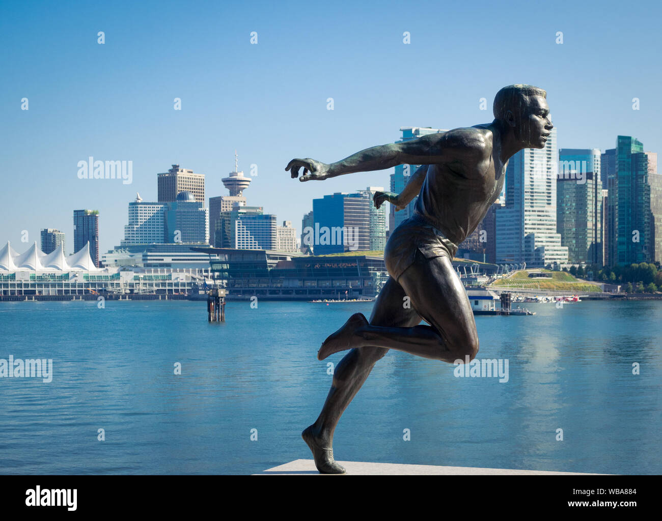 Eine Skulptur von kanadischen Leichtathletik star Harry Jerome im Stanley Park mit Skyline von Vancouver. Vancouver, British Columbia, Kanada Stockfoto