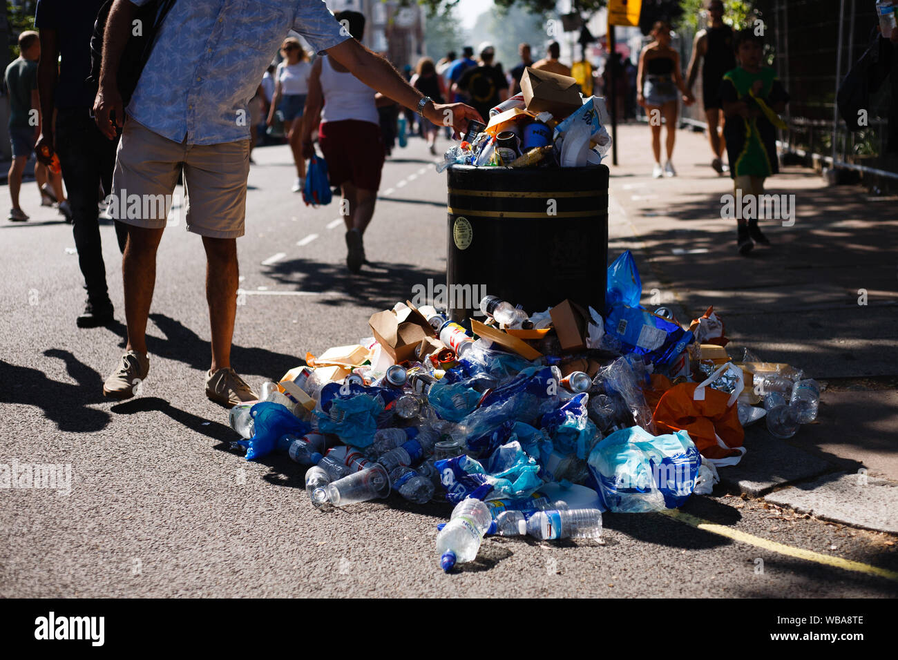 London, Großbritannien. 25 Aug, 2019. Ein Mann fügt ein Stück Müll eine Überfließende bin während der Eröffnung Tag der 2019 Notting Hill Carnival. Bis zu eine Million Menschen werden erwartet, durch die Straßen von Notting Hill zu packen und den umliegenden Gebieten im Laufe der zweitägigen Veranstaltung. Die jährliche Feier des afro-karibischen Kultur nimmt jeder Platz August Bank Holiday Wochenende. Credit: SOPA Images Limited/Alamy leben Nachrichten Stockfoto