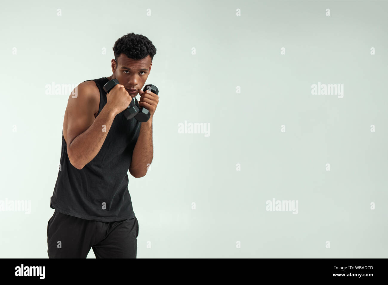 Perfekten Körper. Muskulösen jungen afrikanischen Mann Training mit Kurzhanteln, während gegen grauen Hintergrund stehen. Studio gedreht. Sport Konzept Stockfoto