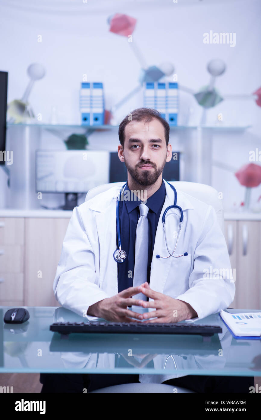 Jung und intelligent Arzt in seinem Kabinett trägt einen weißen Kittel und Stethoskop. Selbstbewussten jungen Arzt. Freundliche Arzt. Stockfoto