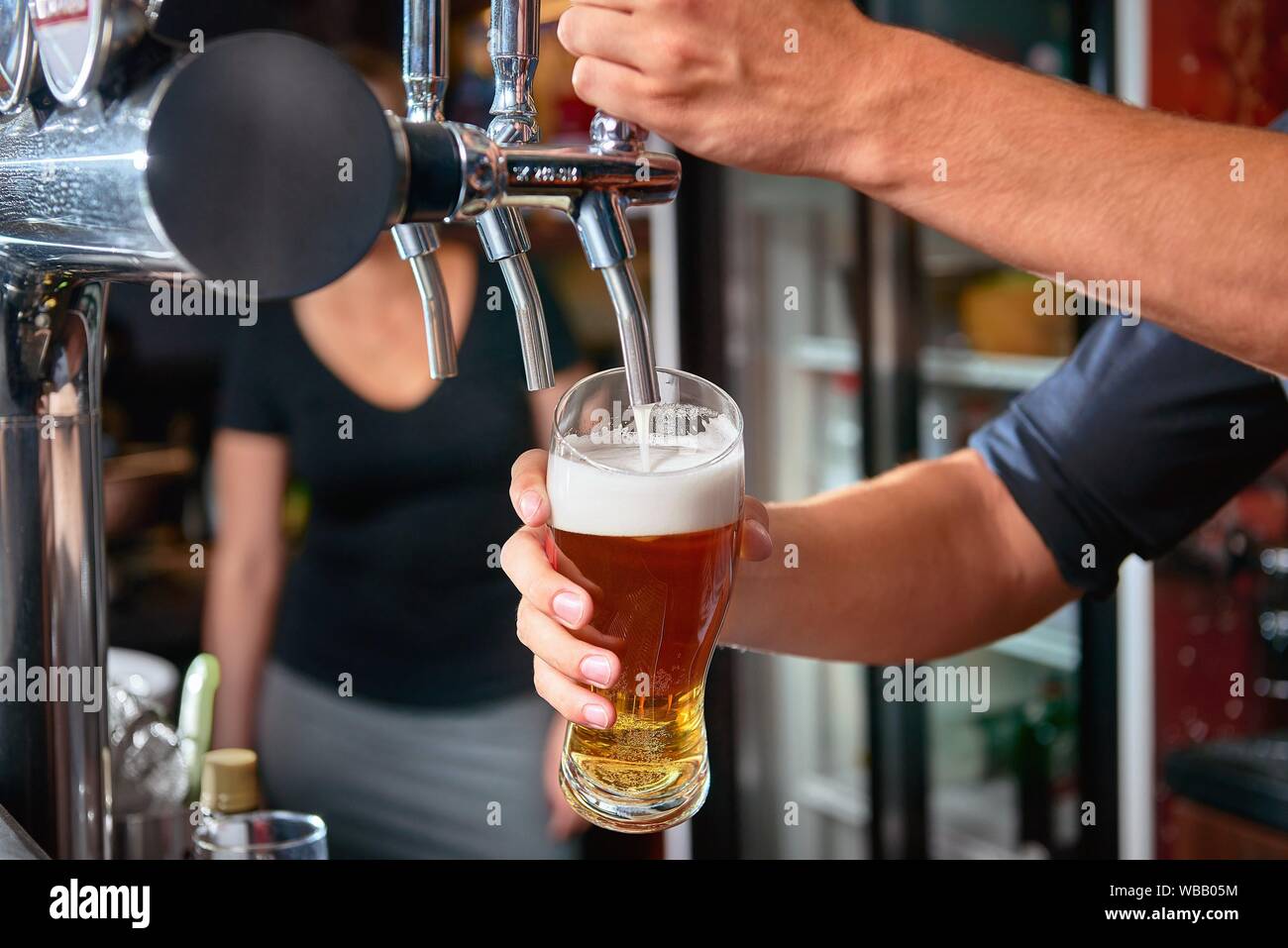 Barkeeper Bier zapfen von hinten Leiste tippen. Verschwommene Frau im  Hintergrund. Kopieren Sie Platz Stockfotografie - Alamy