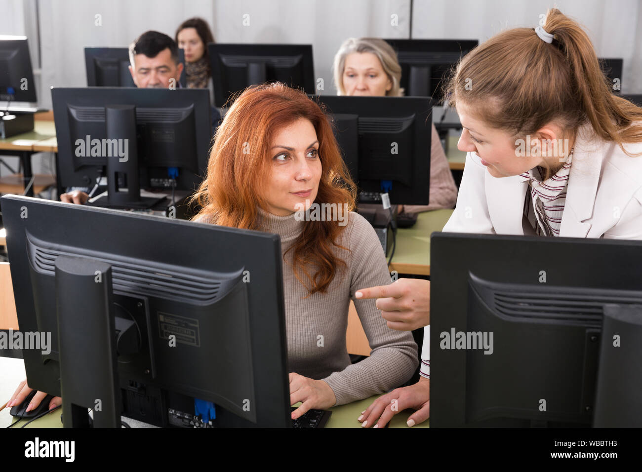 Junge weibliche Lehrer erklären, Computerkenntnisse zu reife Frau in der Klasse Stockfoto