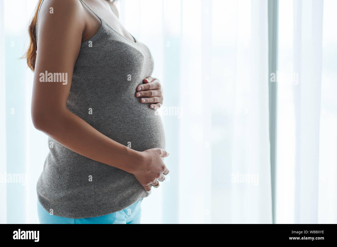 Zugeschnittenes Bild der jungen Frau in Grau top berühren Ihr Baby stoßen, wenn man gegen die grossen Fenster Stockfoto