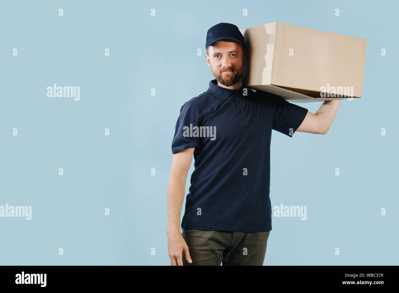 Freundliche Lieferung Mann in Uniform hält großen Karton auf seiner Schulter Stockfoto