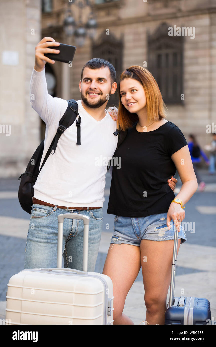 Lächelnde amerikanische weibliche und männliche stehend mit Gepäck auf der Straße und Unter selfie Stockfoto