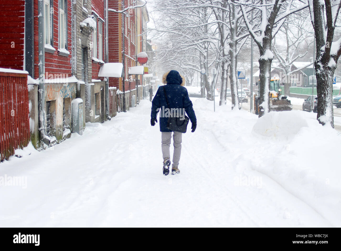 Schneereiche Winter Szene in der Stadt. Schneefall in einer kleinen Straße mit bunten Holzhäuser und ein Mann in Estland, Tallinn Stockfoto