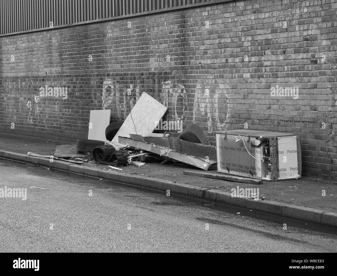 Urban Schuttplatz, Abfall illegal entsorgt auf einem Gehsteig neben einer Wand mit Graffiti in der Stadt und Umgebung. Stockfoto