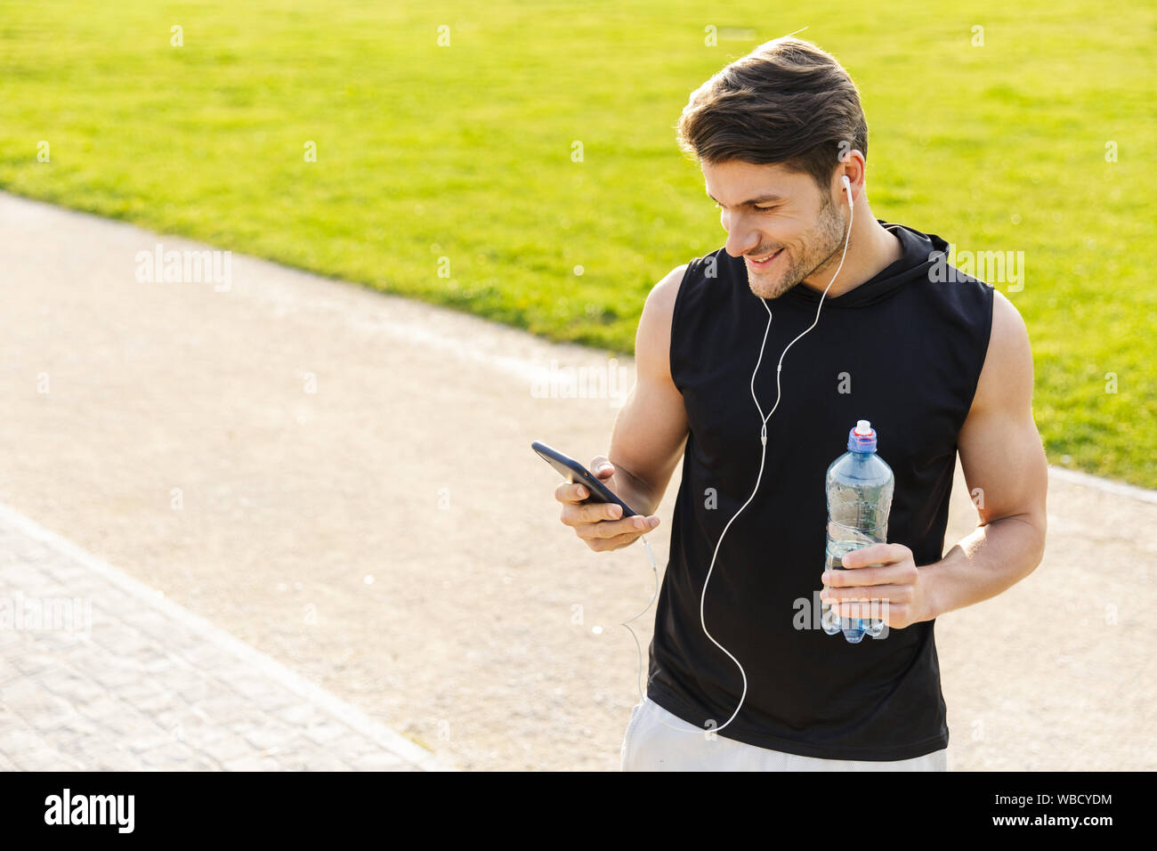Bild von glücklichen Menschen in Sportkleidung Trinkwasser und Holding Handy während der Ausführung mit Ohrhörer in Green Park im Freien Stockfoto