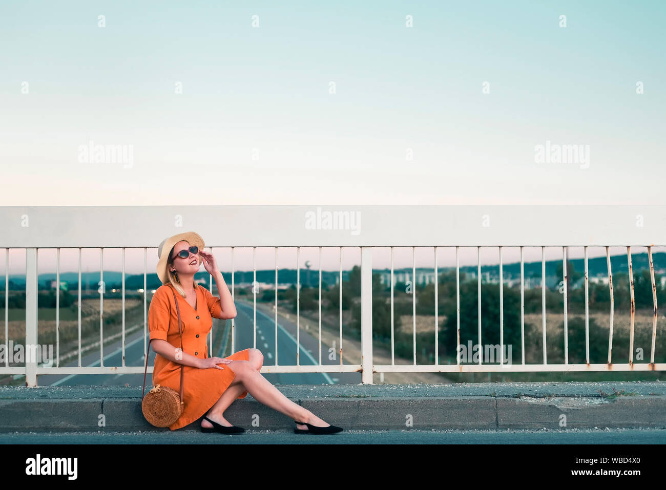 Junge Frau in orange Kleid sitzt auf der Brücke Stockfoto