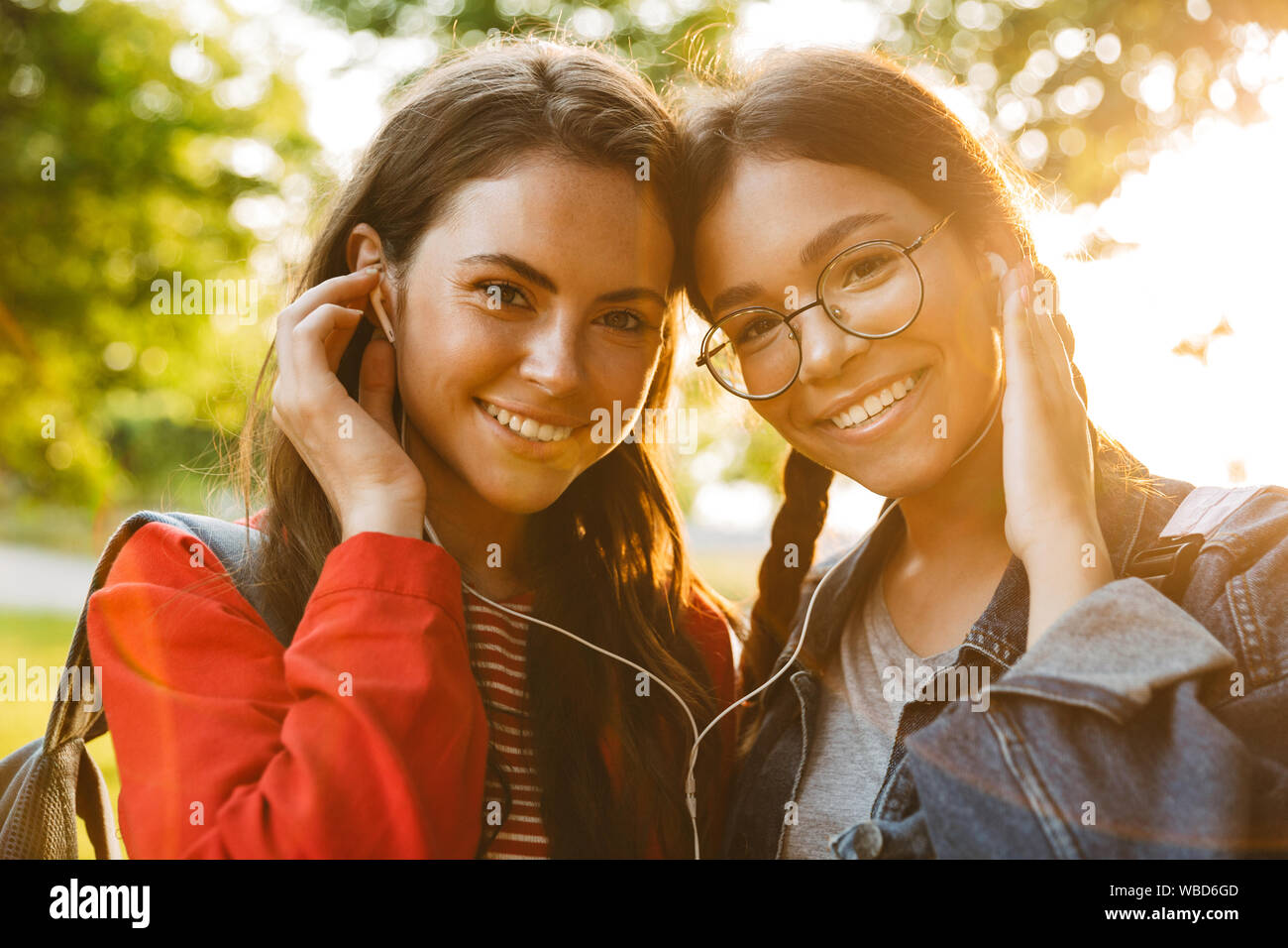 Bild Nahaufnahme von zwei netten Mädchen Studenten tragen Rucksäcke mit Ohrhörer und Kamera beim Gehen im Green Park Stockfoto