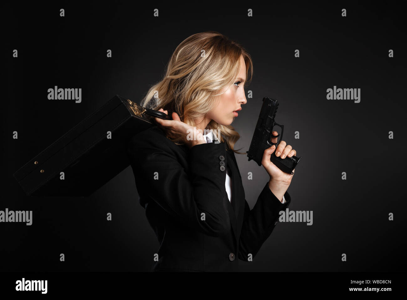Seitenansicht Porträt einer wunderschönen zuversichtlich, blonde Frau in formelle Kleidung über schwarzen Hintergrund isoliert stehenden gekleidet, Besitz einer Waffe, während Stockfoto