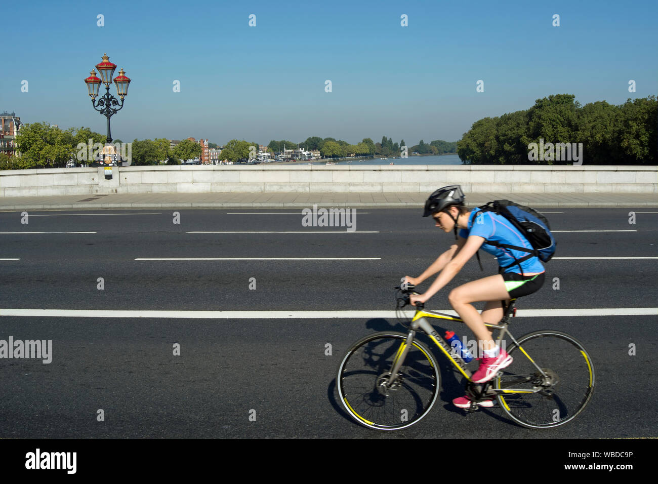 Weibliche Radfahrer Radfahren von Norden nach Süden auf der Putney Bridge, London, England, mit der Themse im Hintergrund Stockfoto