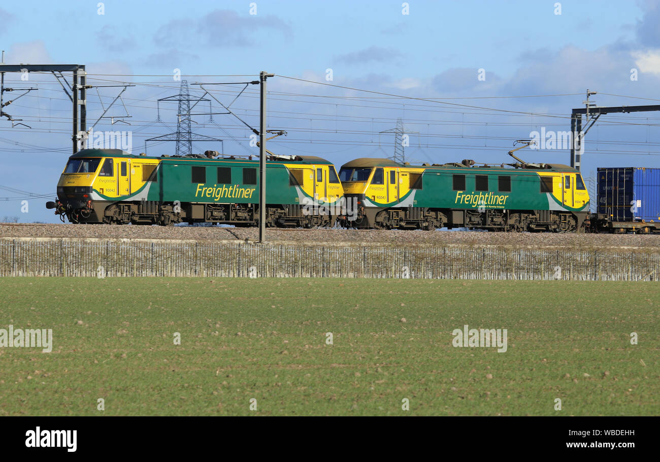 Zwei Klasse 90 elektrische Lokomotiven, schleppen Sie einen Behälter mit einem Güterzug entlang der West Coast Main Line, Staffordshire, England, im Jahr 2018. Stockfoto