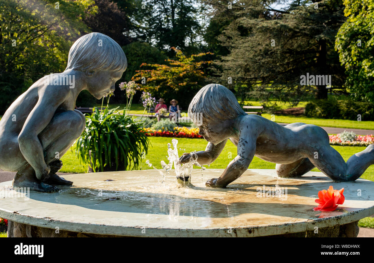 Statuen der Kinder am Brunnen, Frauen ruht auf einer Parkbank im Hintergrund bei sehr heißem Wetter, Bank Holiday Montag, Valley Gardens, Harrogate, UK, 26. August 2019 Stockfoto