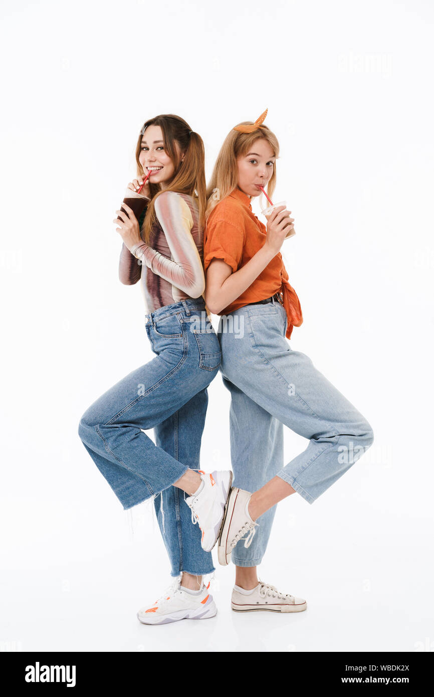 Foto von zwei netten Mädchen tragen bunte Kleidung Rücken an Rücken beim Trinken von Soda Getränke auf weißem Hintergrund Stockfoto