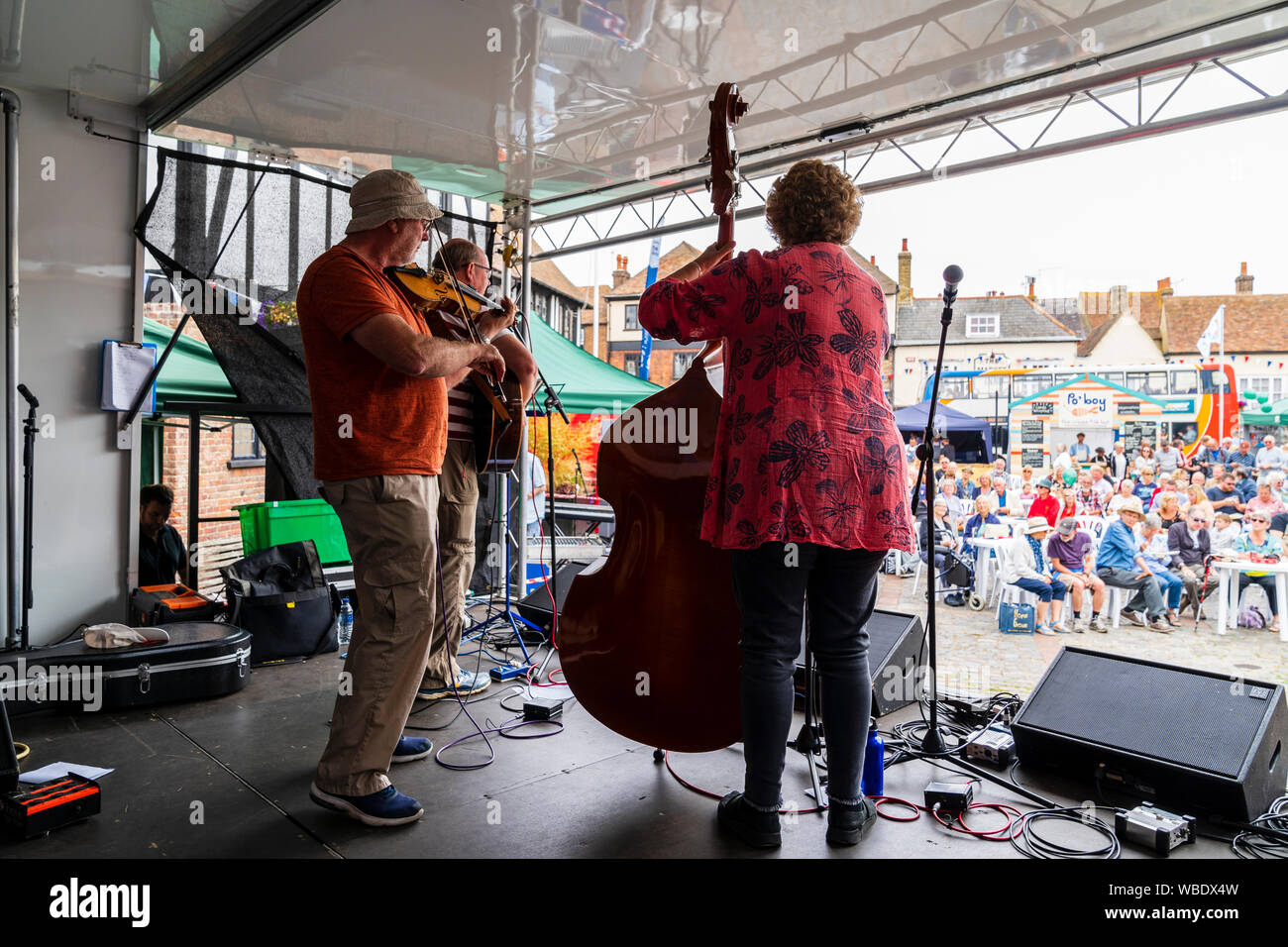 Sandwich Folk und Ale-Festival. Folk music group Cajun Boogaloo auf der Bühne auf dem Marktplatz mit sitzenden Publikum zu beobachten. Von hinten Trio gesehen. Stockfoto