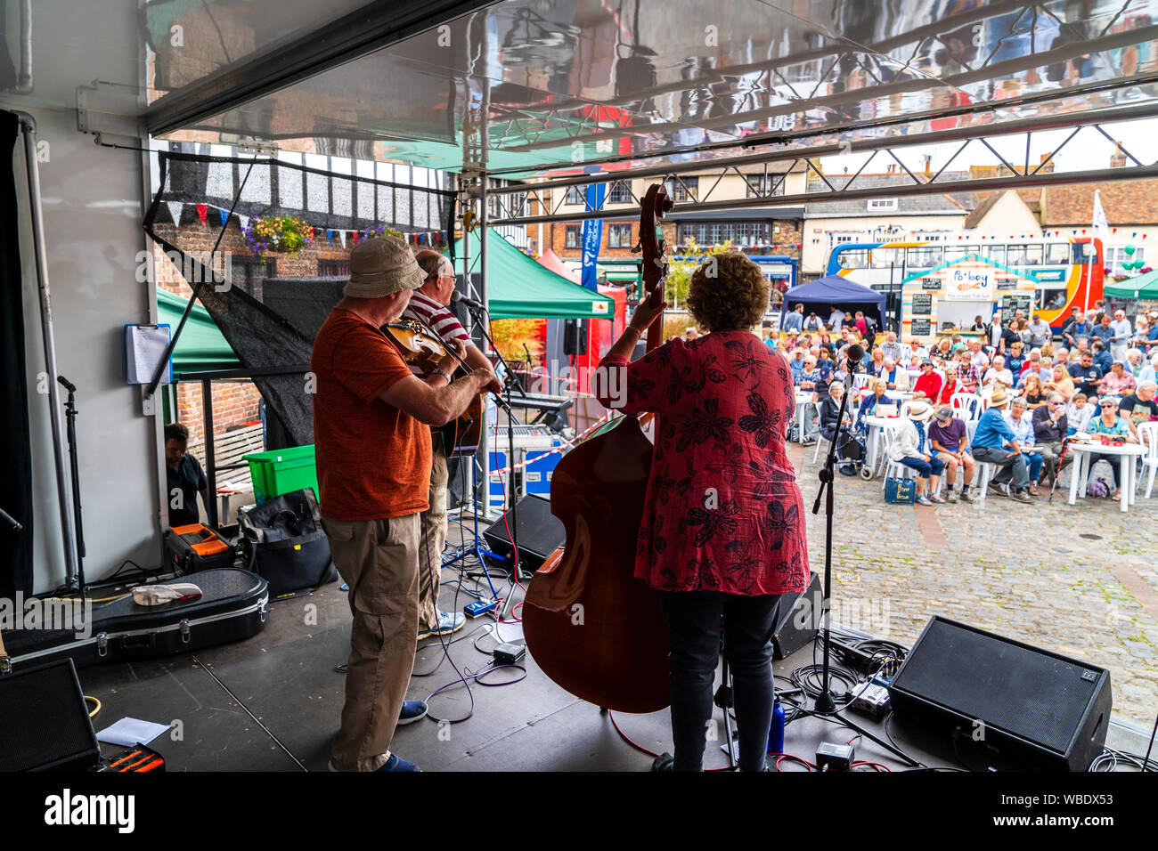 Sandwich Folk und Ale-Festival. Folk music group Cajun Boogaloo auf der Bühne auf dem Marktplatz mit sitzenden Publikum zu beobachten. Von hinten Trio gesehen. Stockfoto