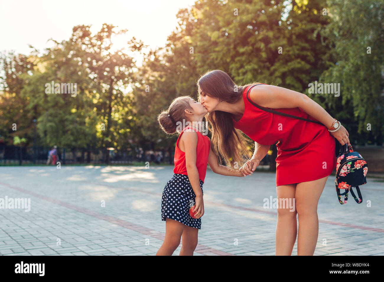 Glückliche Mutter treffen ihre Töchter nach dem Unterricht im Freien Grundschule. Familie küssen. Zurück zum Konzept der Schule Stockfoto