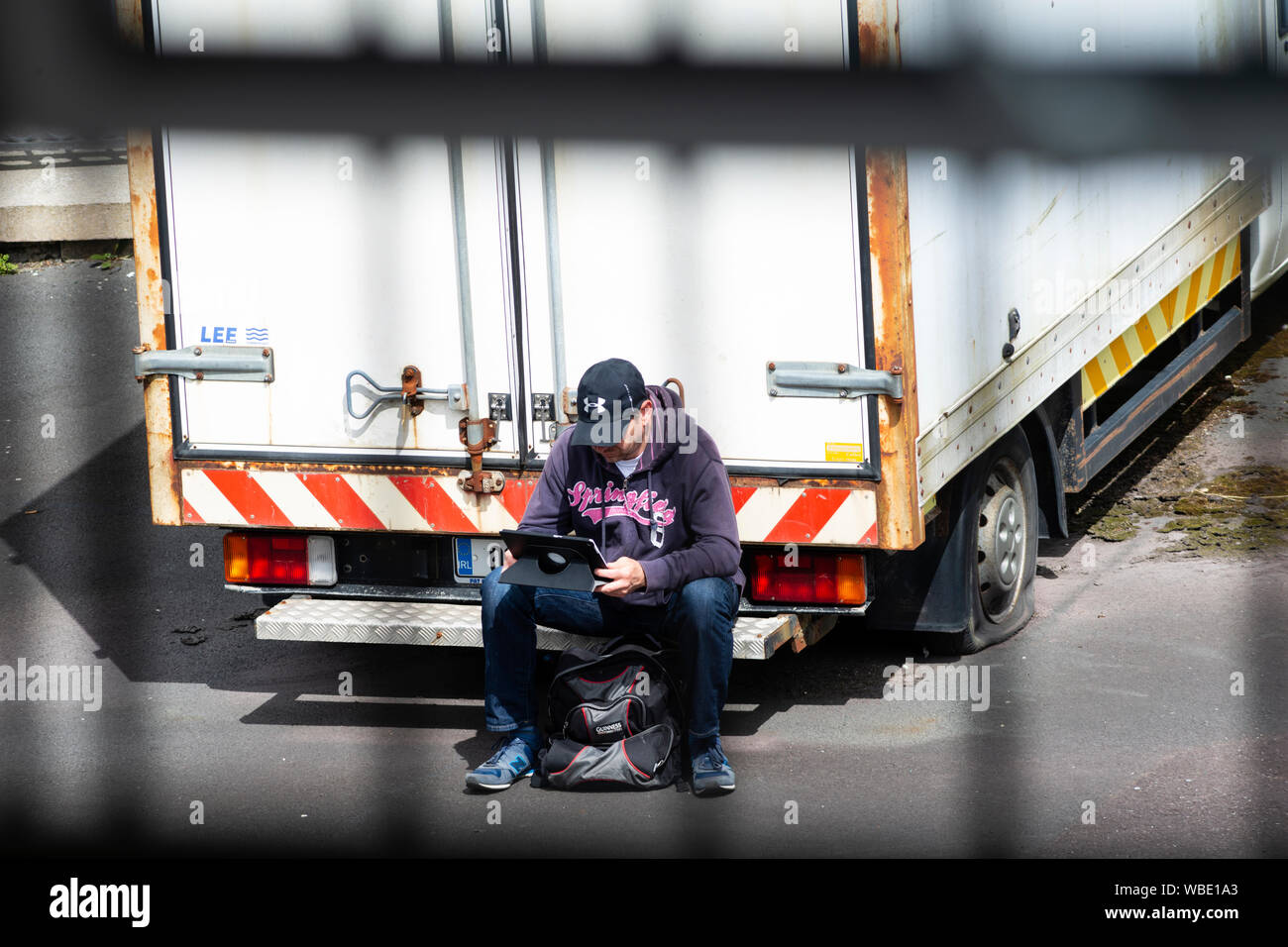 Mann mit Laptop sitzen auf der Rückseite eines verlassenen Lieferwagen in privaten Parkplatz versucht, einen kostenlosen WLAN-Signal von der in der Nähe von Gebäude zu fangen. Stockfoto