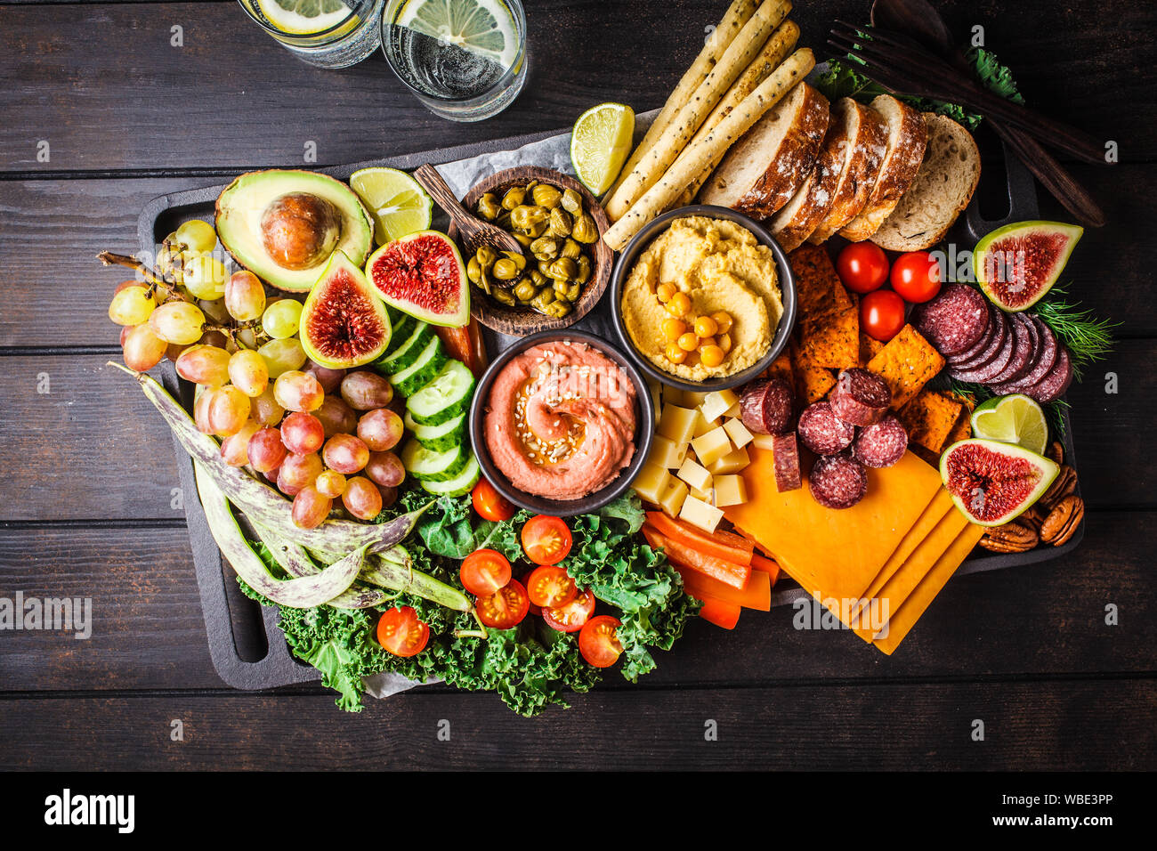 Fleisch und Käse Vorspeise Platter. Wurst, Käse, Hummus, Gemüse, Obst und Brot auf einem schwarzen Fach, dunklen Hintergrund. Stockfoto