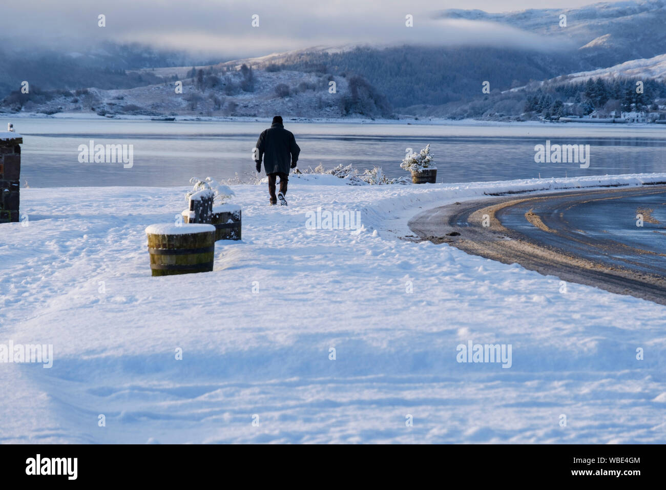 Solo Männer gehen auf Schnee lochside Pfad in Lochcarron, Wester Ross, NW Highlands von Schottland Stockfoto