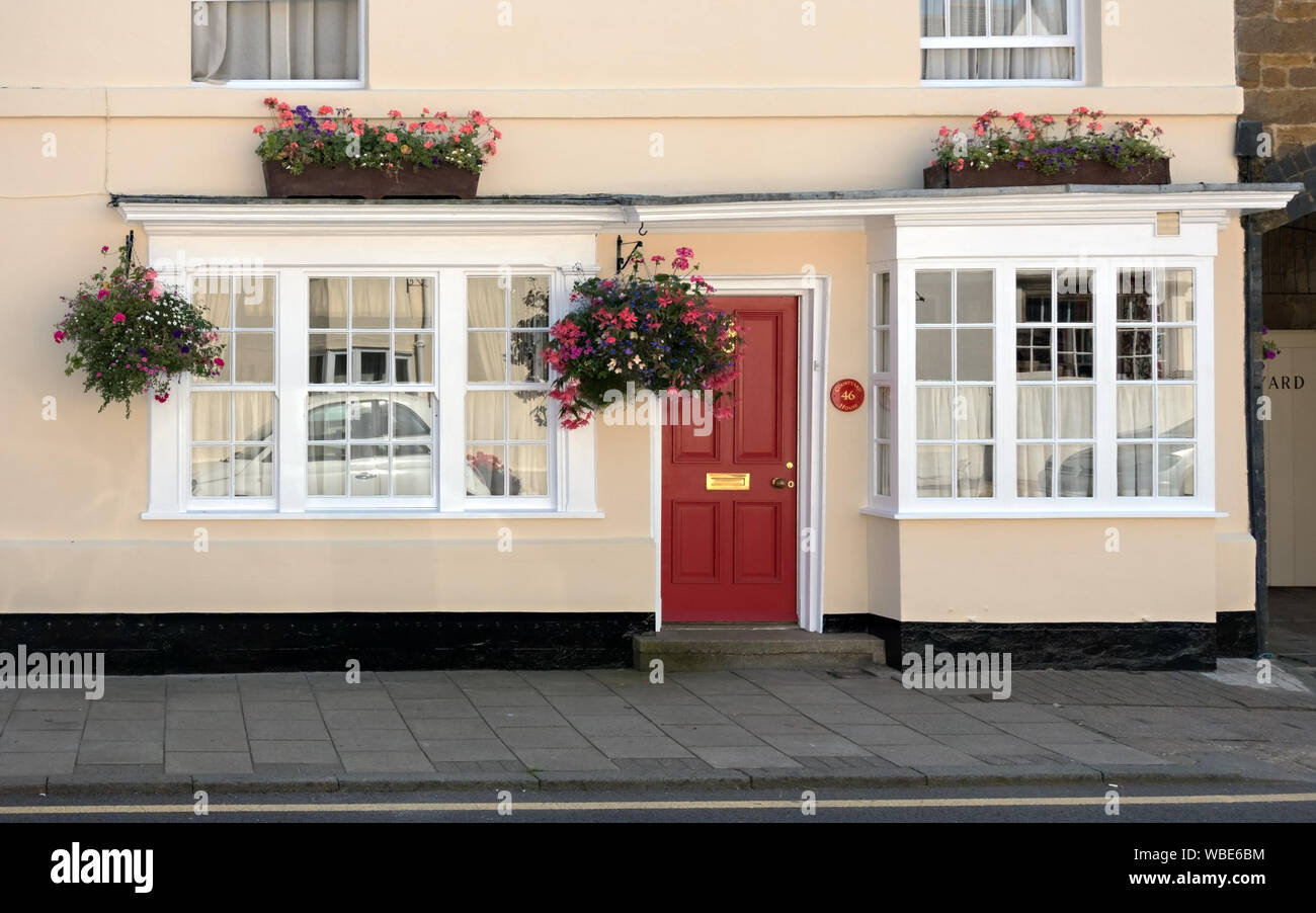 Frisch cremefarbenen Haus/Haus mit roten Haustür gemalt, weiße Schiebefenster, hängende Körbe und Pflanzer, Uppingham, England, UK. Stockfoto
