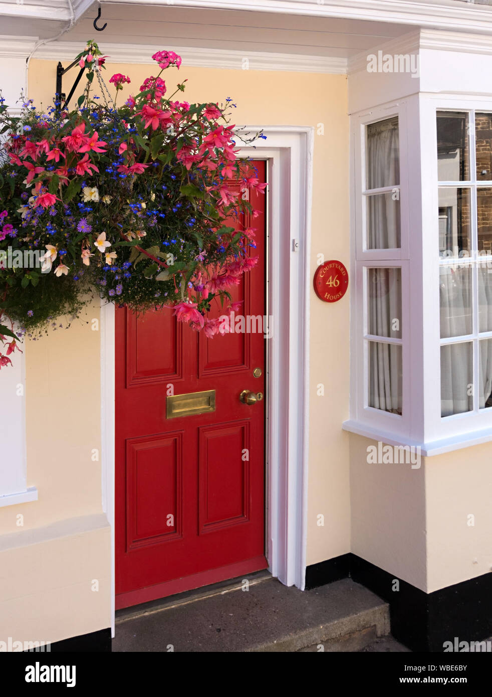 Frisch cremefarbenen Haus/Haus mit roten Haustür gemalt, weiße Schiebefenster und hängenden Korb, Uppingham, England, UK. Stockfoto