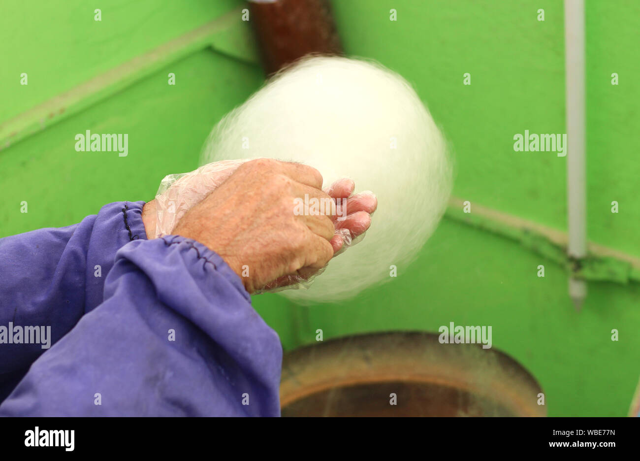 Hausgemachte Prozess, Zuckerwatte. Hände von einem alten Mann mit einem Stock mit Zuckerwatte Stockfoto
