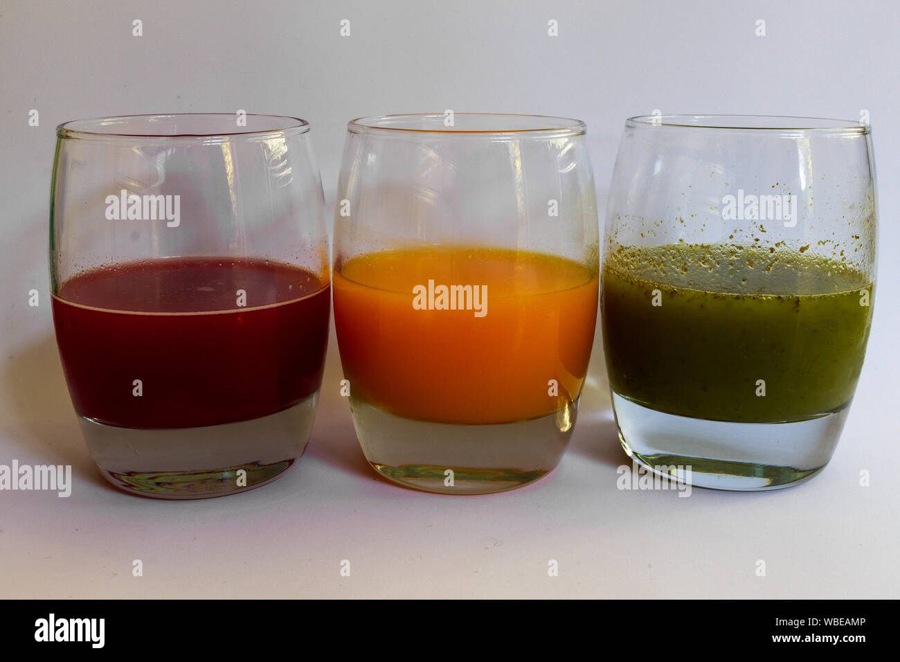 Drei Gläser aufgereiht mit rotem Traubensaft, Orangensaft und grünes Gemüse Saft in Ampel Sequenz Stockfoto