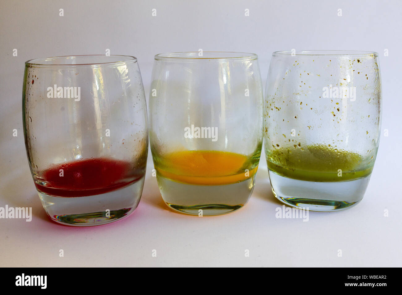 Drei fast leere Gläser aufgereiht mit rotem Traubensaft, Orangensaft und grünes Gemüse Saft in Ampel Sequenz Stockfoto