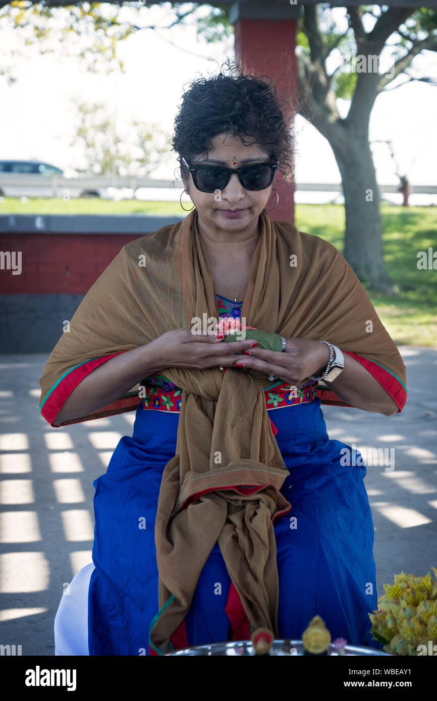 Eine attraktive Hinduistische Frau hält eine Blume bei einem Geburtstag Service im Freien an einem Strand aus Jamaica Bay in Queens, New York City. Stockfoto