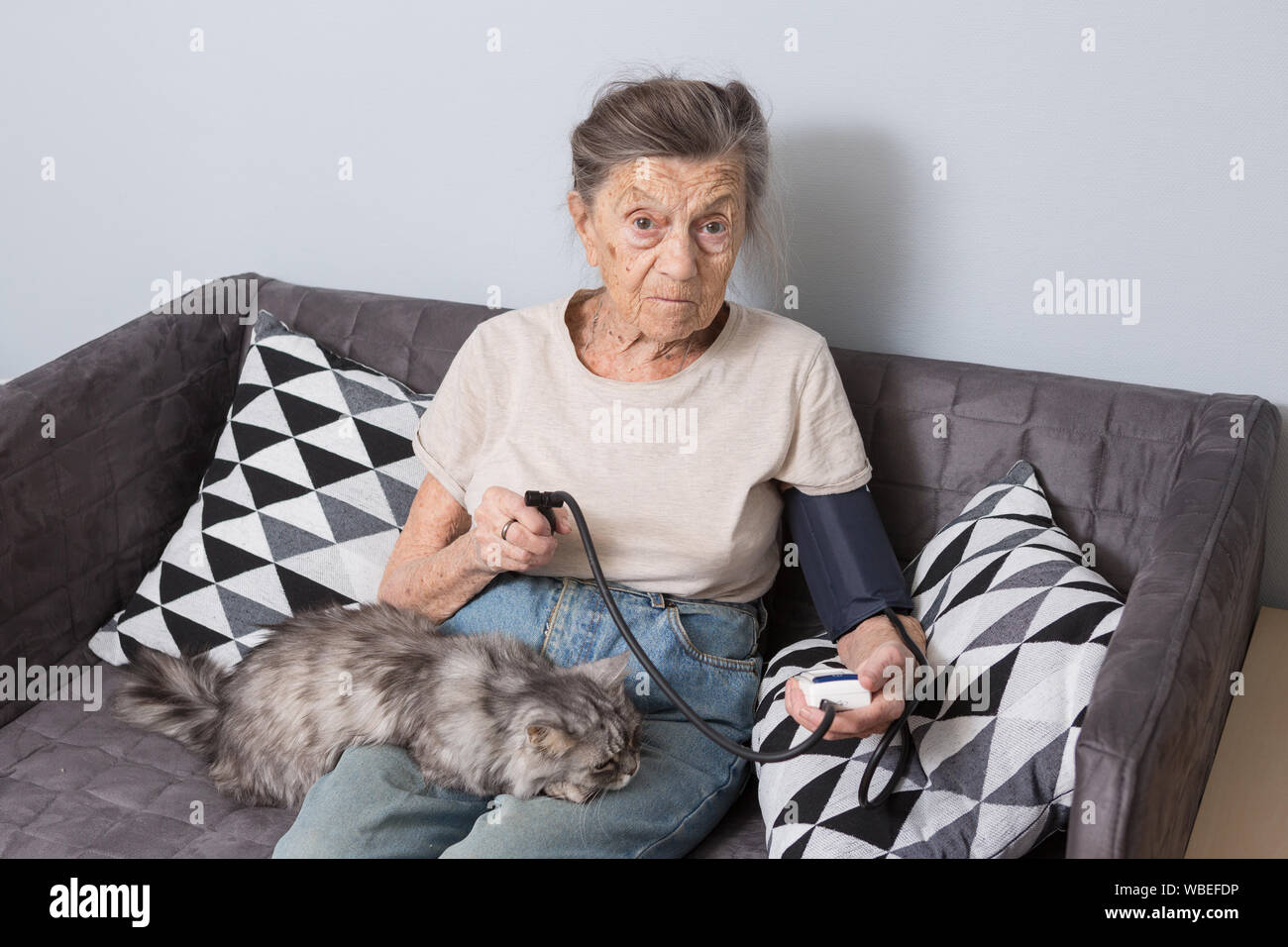 Das Thema ist sehr alte Person und gesundheitliche Probleme. Ein älterer kaukasische Frau, 90 Jahre alt, mit Falten und graue Haare, sitzt zu Hause auf dem Sofa mit Haustier Katze Stockfoto