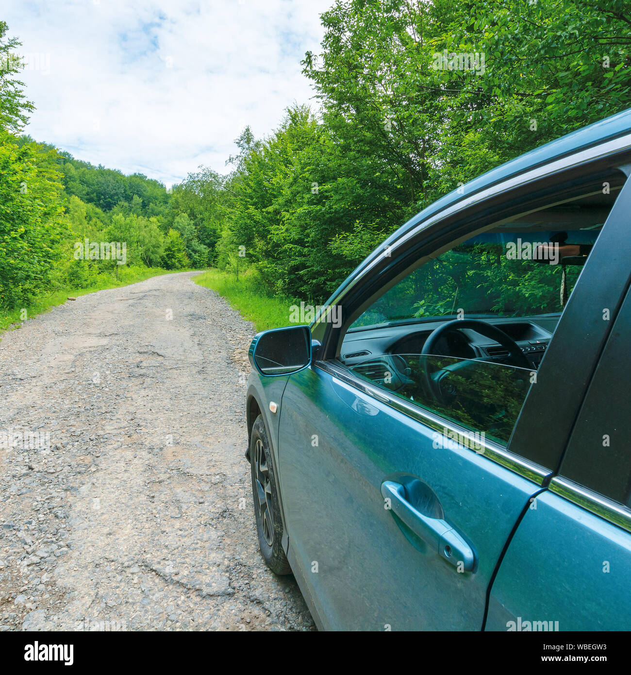 Suv auf der alten Forststraße. Cyan Blau Fahrzeug auf dem gebrochenen Asphalt Weg bergauf unter Bäumen geparkt. Blick vom Fahrer tür und Spiegel. d verloren Stockfoto