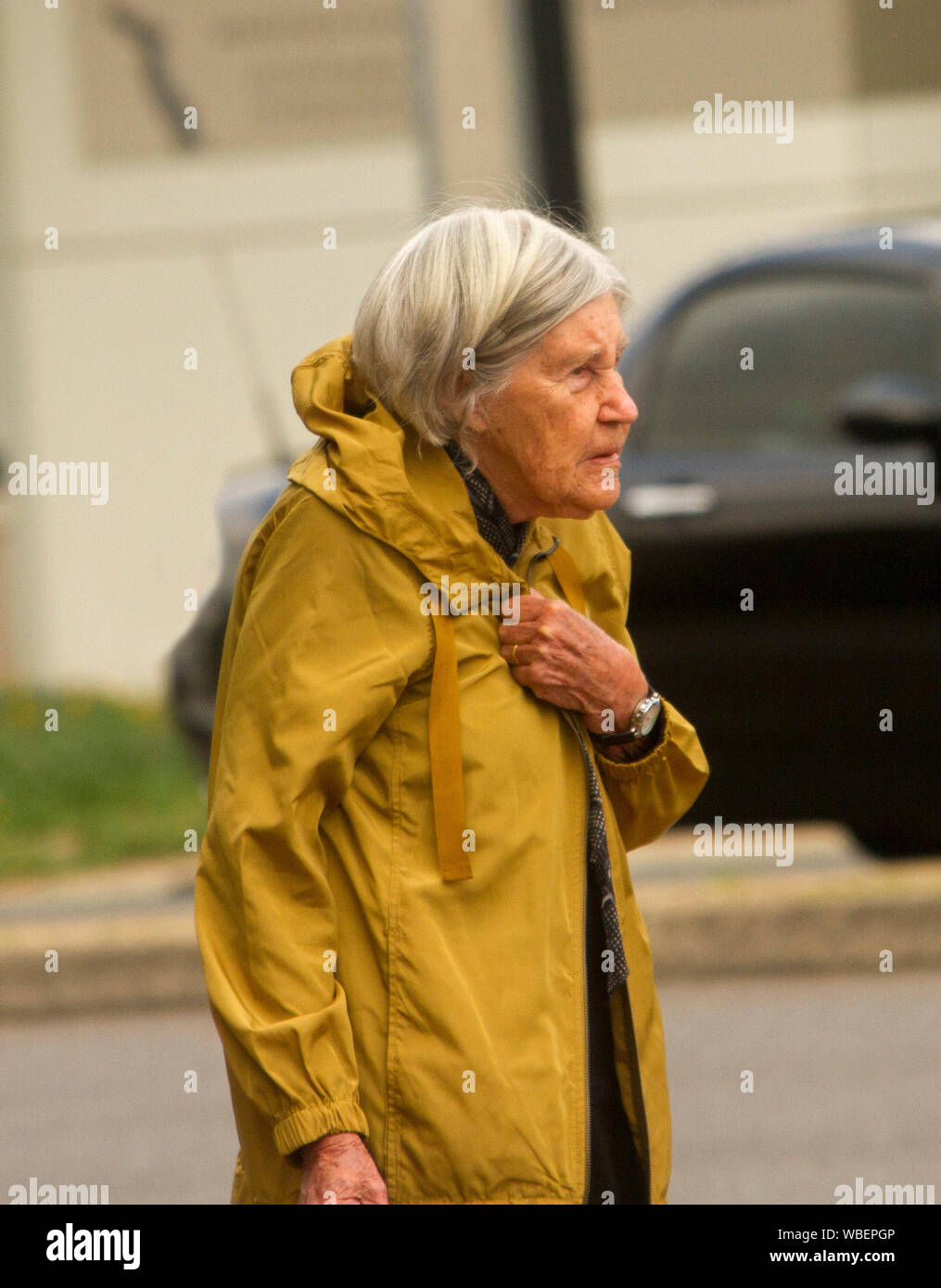 Ältere Frau mit dem grauen Haar und gelben Regenmantel Frieren am Tag eines miserablen Winter Stockfoto