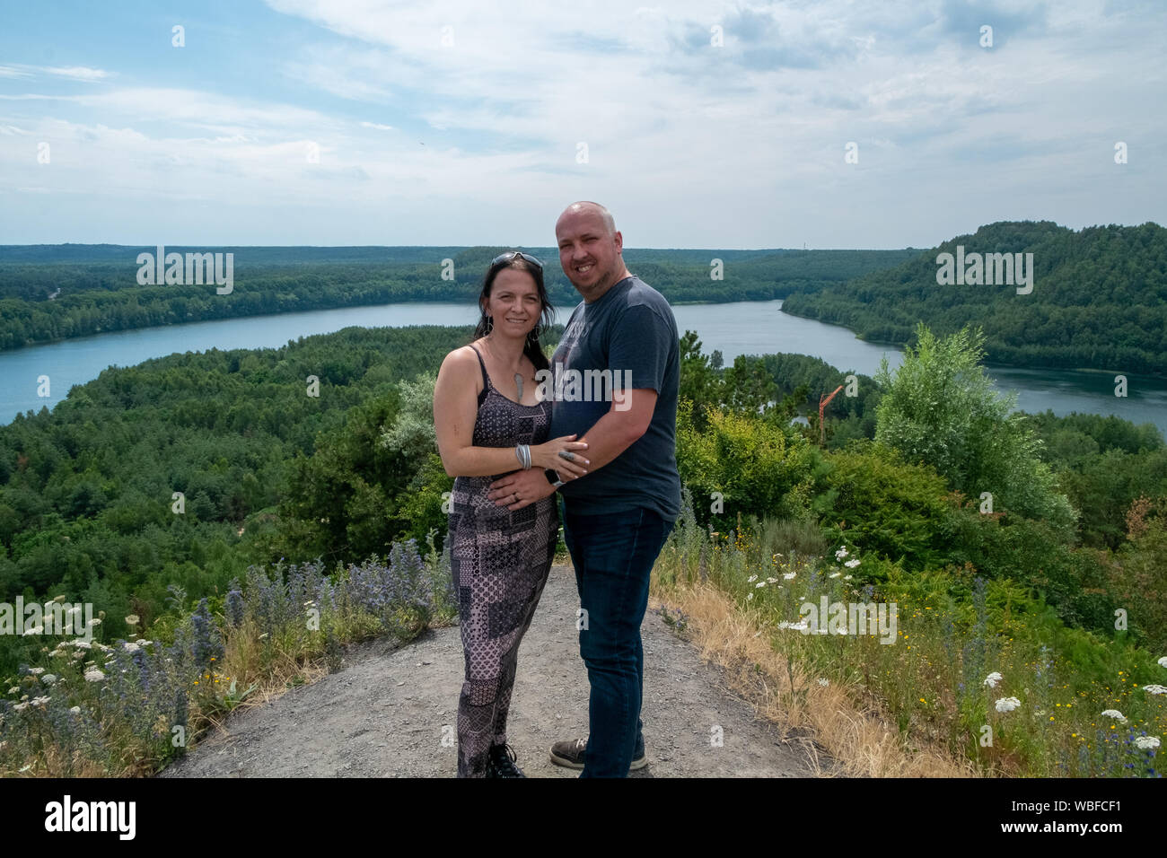 Paar von 30-40 Jahre alt im Freien umarmen und hoch auf einem Hügel mit einem Fluss durch den Wald läuft im Hintergrund Stockfoto