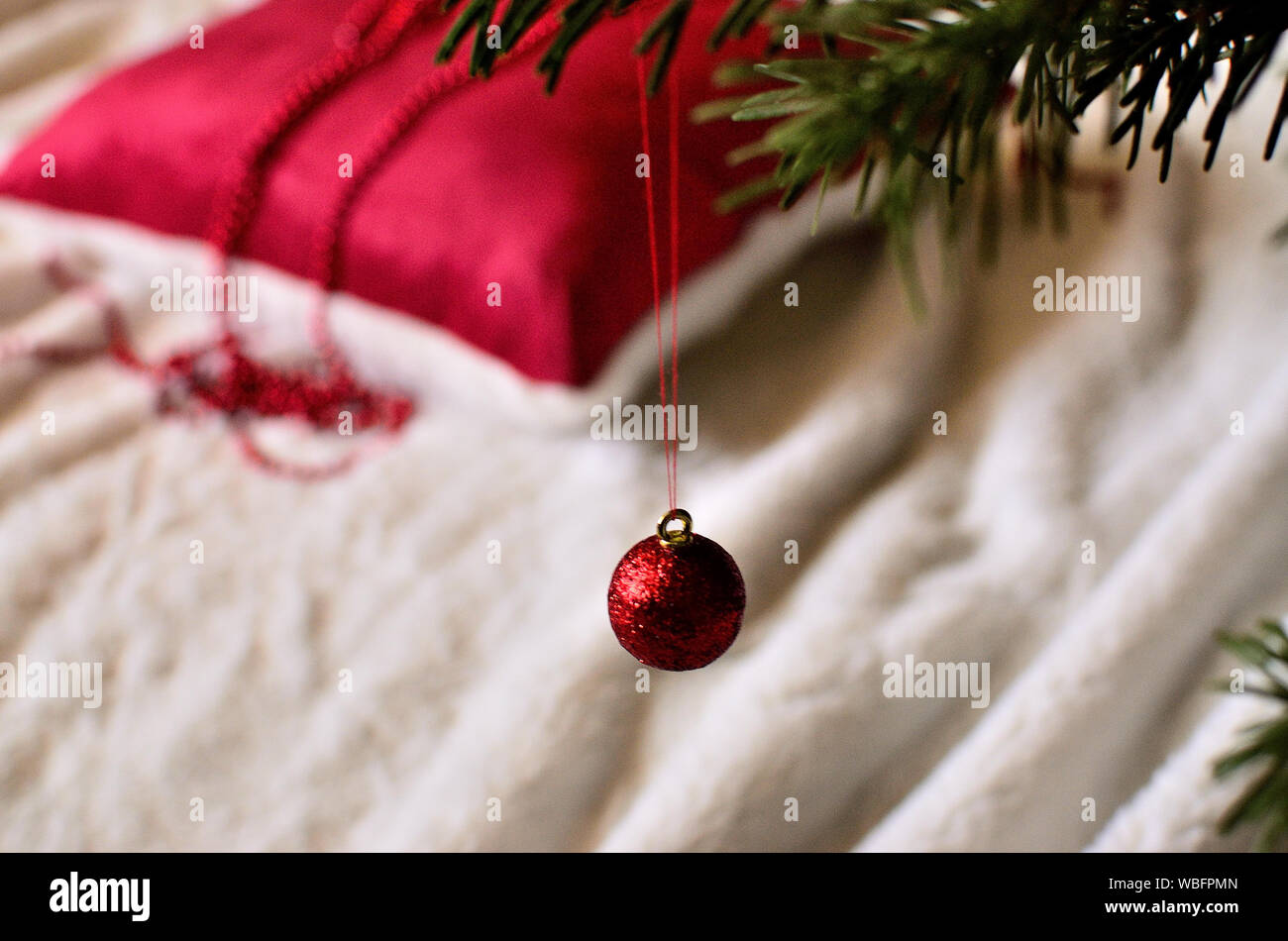 Ein rotes Schmuck am Weihnachtsbaum und ein flauschiges rotes Kissen im Hintergrund. Stockfoto