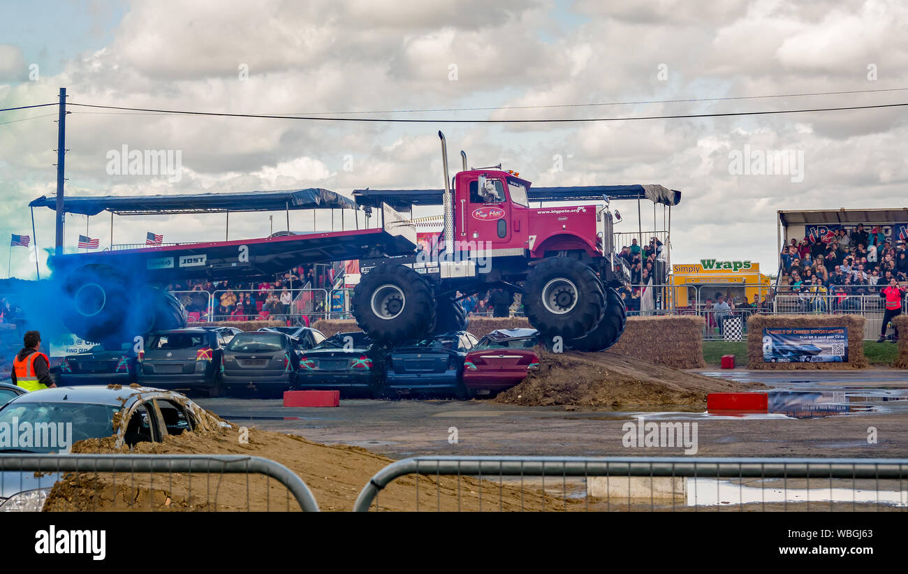 Die Monster truck Big Pete Zerkleinerung ein Auto Stapel während Abschleppen eine maßgeschneiderte kundenspezifische Trailer während einer Demonstration an einem Monster Truck Show Stockfoto