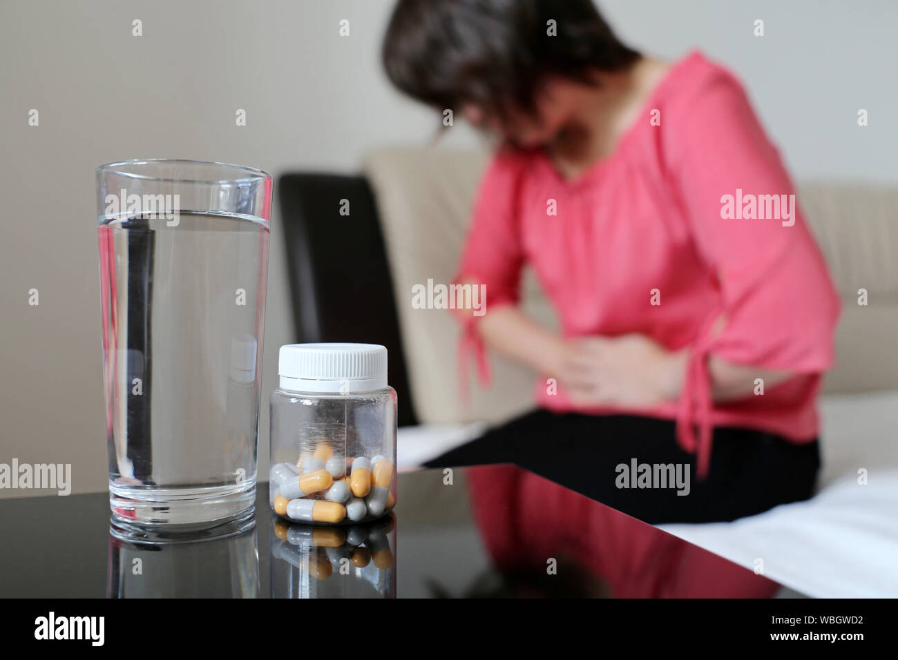 Magenschmerzen, Flasche Pillen und Wasser Glas auf Hintergrund der Frau mit Bauchschmerzen. Mädchen umklammerte ihr Abdomen, Menstruation Konzept Stockfoto