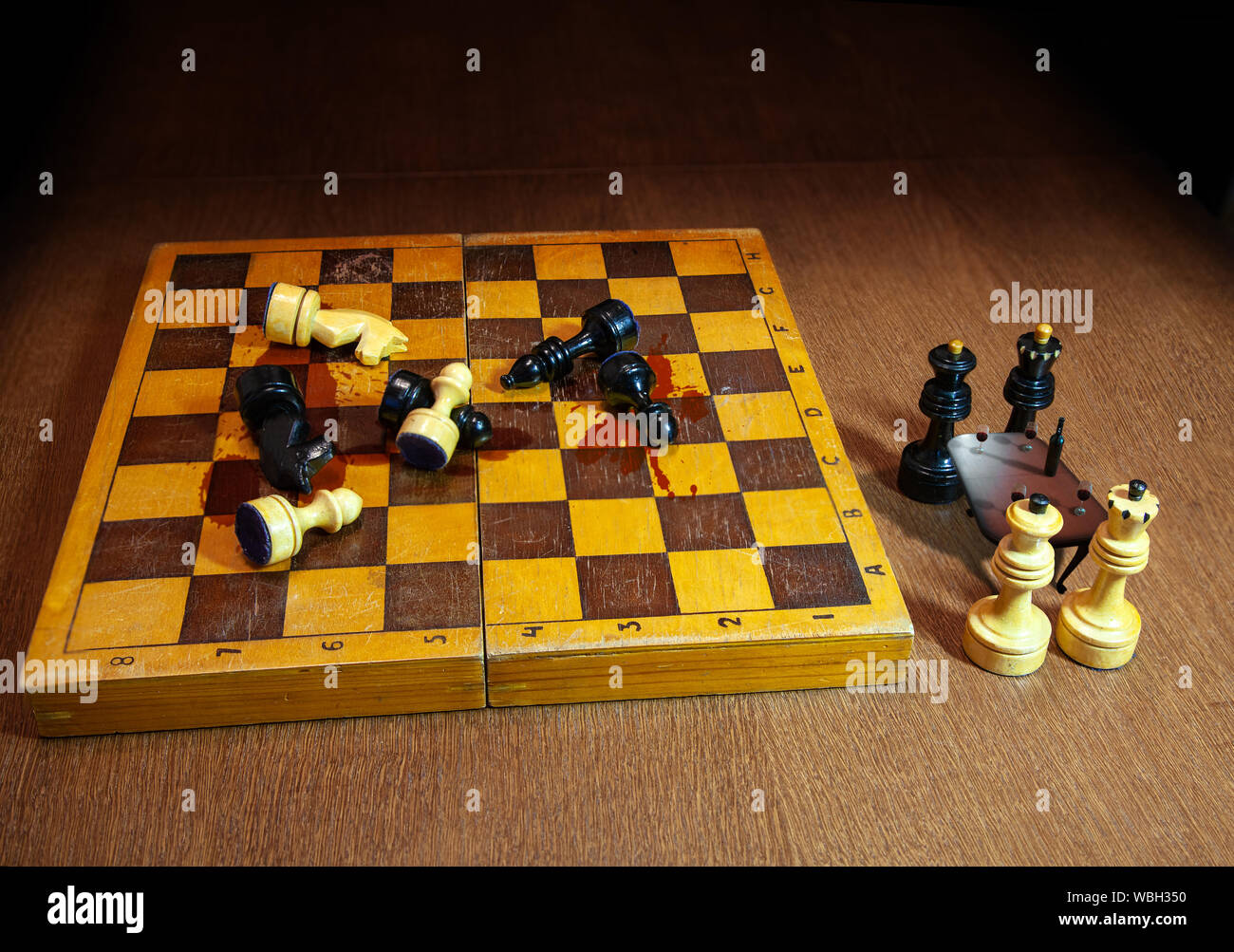 Schach schwarze und weiße Könige und Königinnen feiern mit Gläsern Wein in der Nähe des Schlachtfeldes auf einem Schachbrett Stockfoto