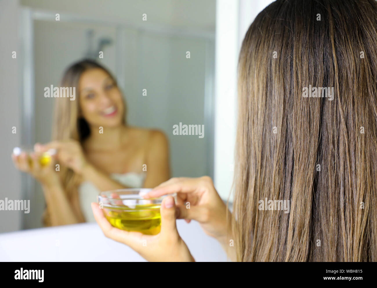 Junge Frau mit Olivenöl Maske für die Haare vor dem Spiegel. Hair Care  Konzept. Fokus auf das Haar Stockfotografie - Alamy