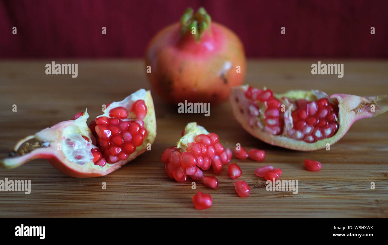 Ein ganzes und ein offener Granatapfel oder die Frucht der Punica granatum enthüllt Cluster von roten, saftigen Samen, faserige arils und Dick und wachsartige Schale Stockfoto