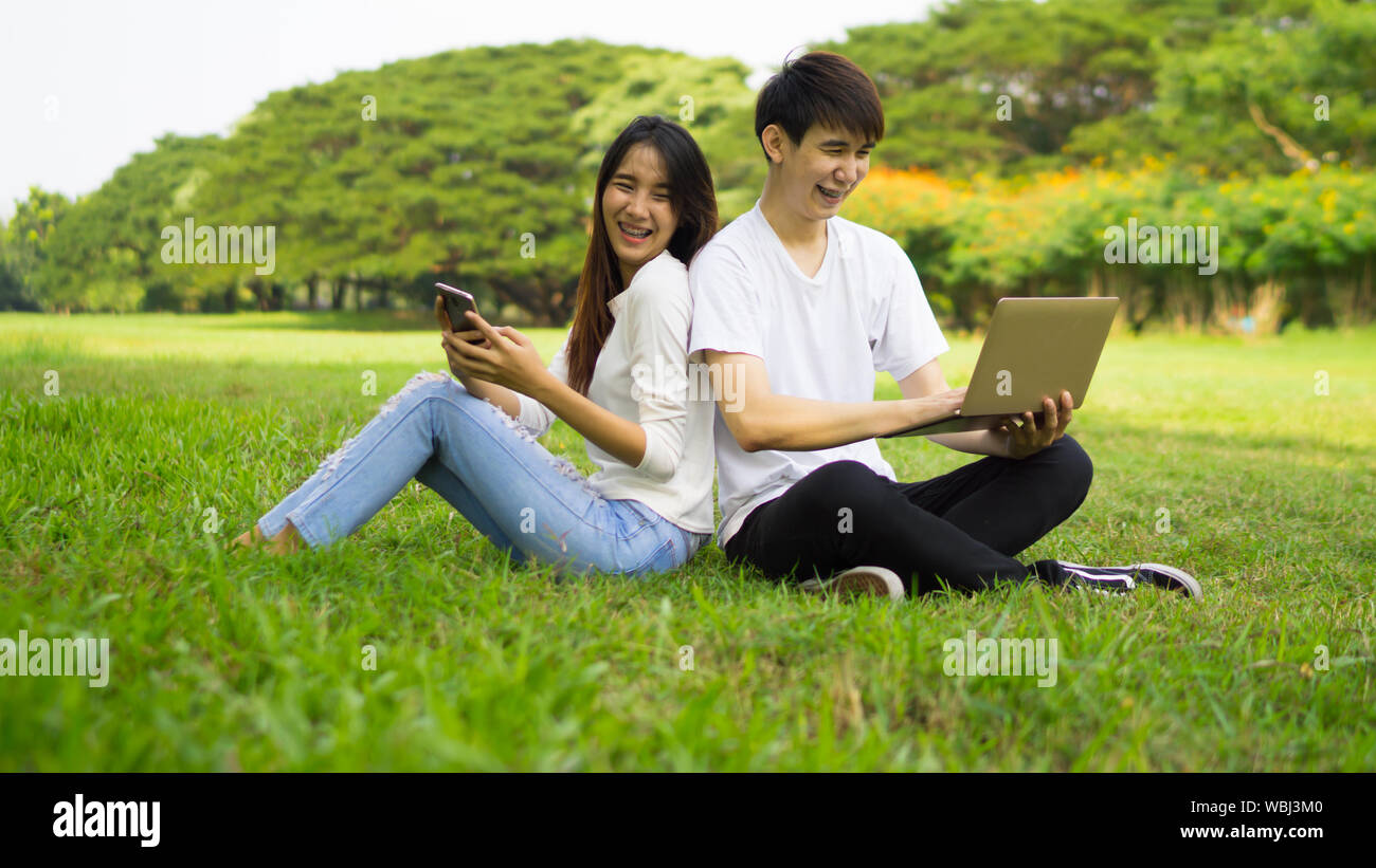 Paar verwenden drahtlose Technologie beim Sitzen auf der Wiese im Park Stockfoto