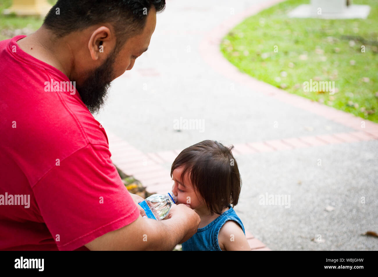 Der bärtige Mann gibt, Wasser zu einem Kleinkind Kind. Asiatische Familie, Elternschaft und Vaterschaft Konzept. Stockfoto