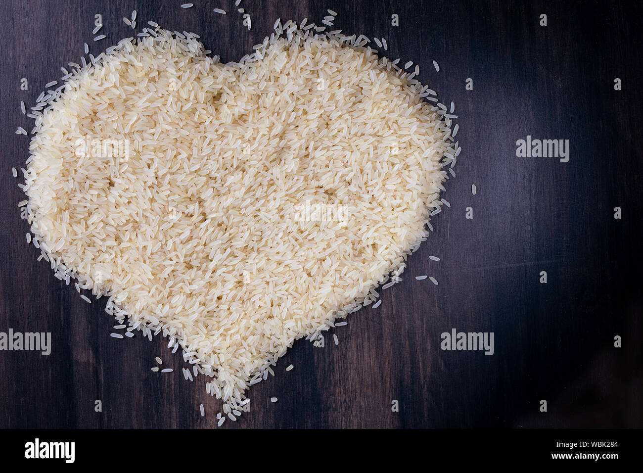 Ansicht von oben Herz Symbol für parboiled Reis auf schwarz Holz Hintergrund Stockfoto