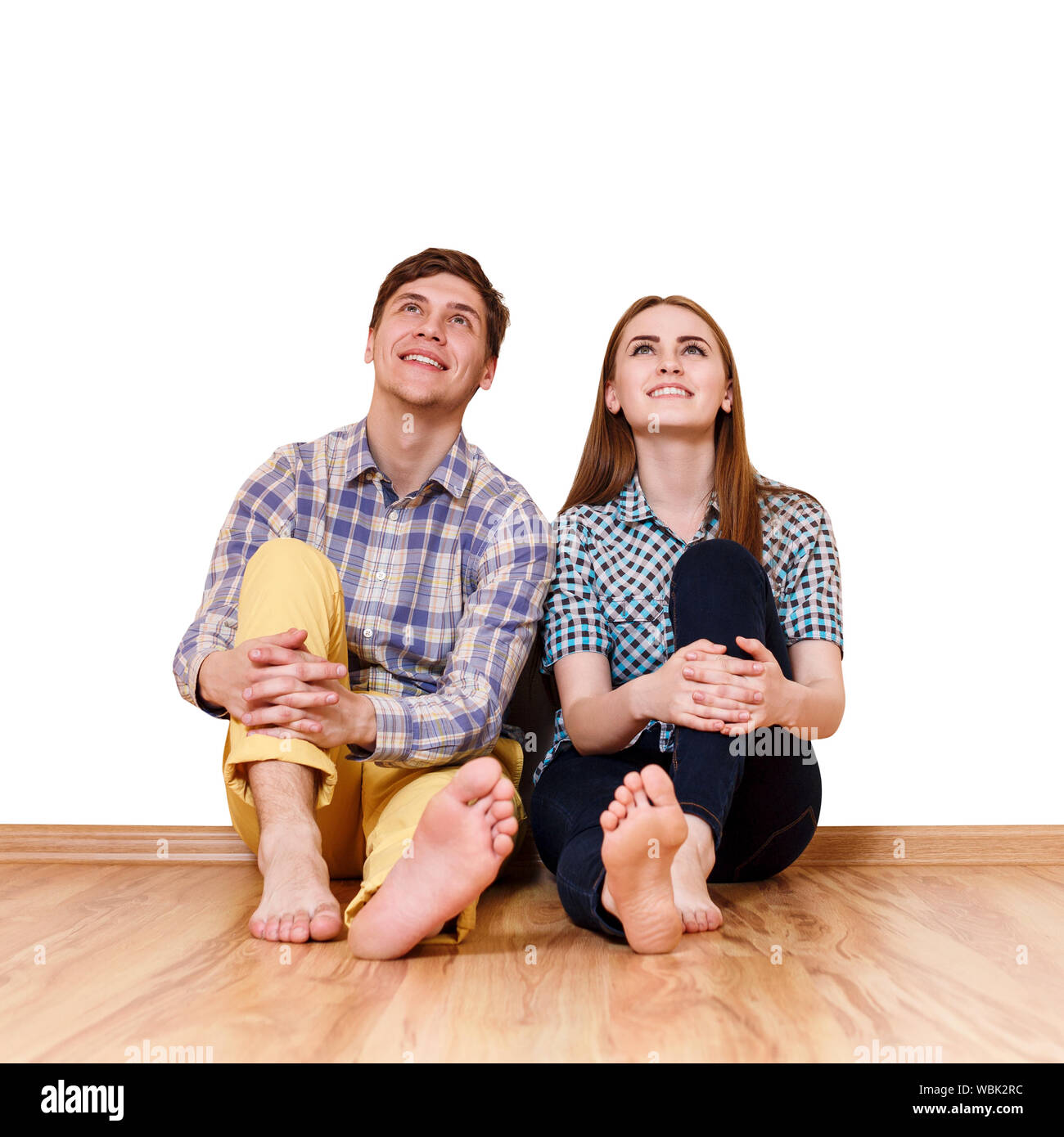 Junge glückliches Paar auf dem Boden sitzend in Ihre neue Wohnung über weiße Wand im Hintergrund. Stockfoto