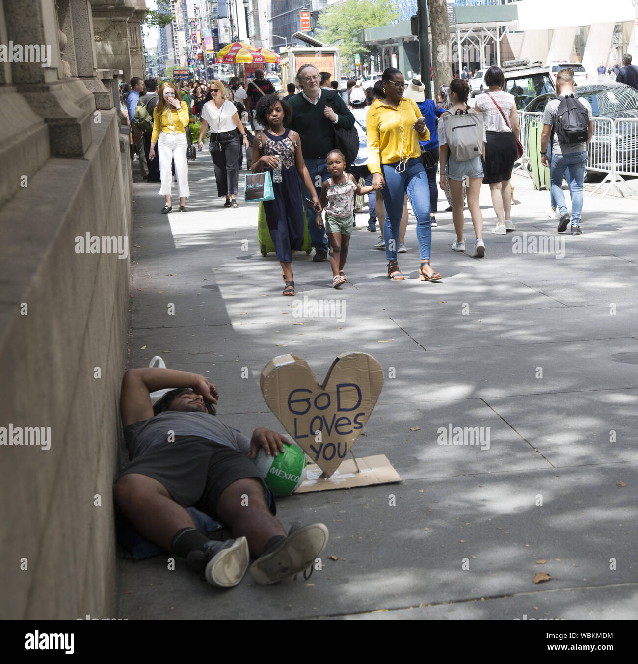 Obdachlosen mit einem Schild: "Gott liebt dich" beruht auf dem Bürgersteig, während die Menschen in Midtown Manhattan entfernt. Stockfoto